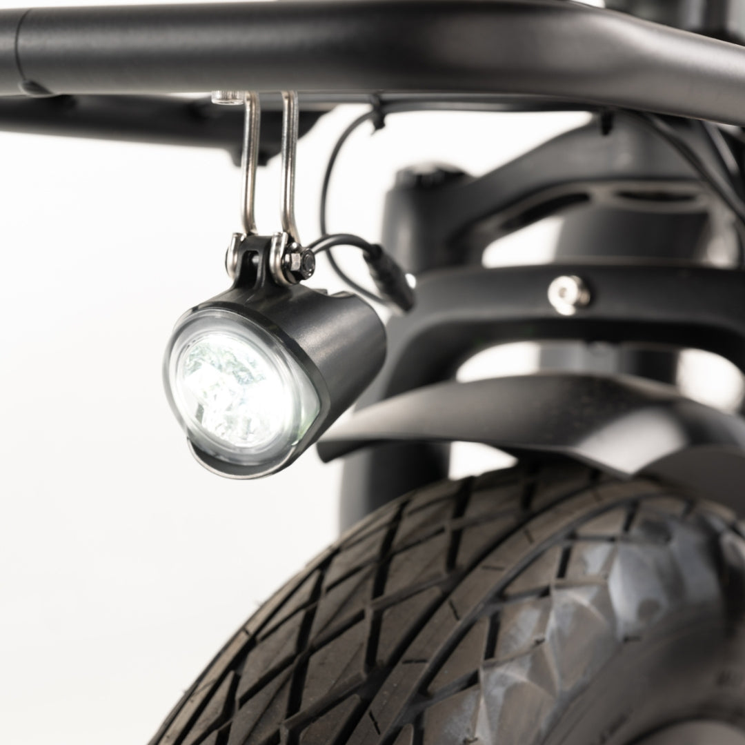 A black electric bicycle front LED headlight mounted beneath a front cargo rack