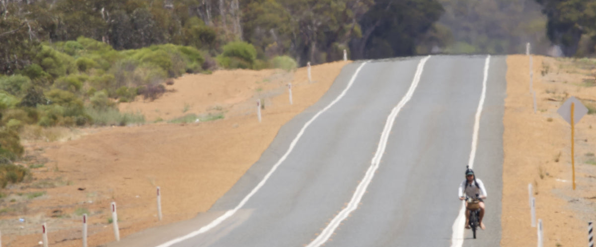 A man riding a Vamos bike along an empty road during a Perth to Bondi journey.