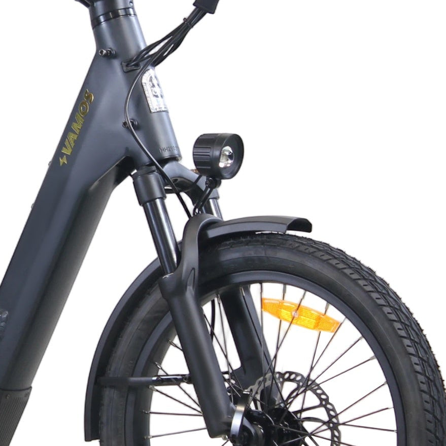 Studio product detail shot showing the front suspension fork, LED headlight, front disc brake, and gold Vamos branding on a dark grey step-through electric bike.