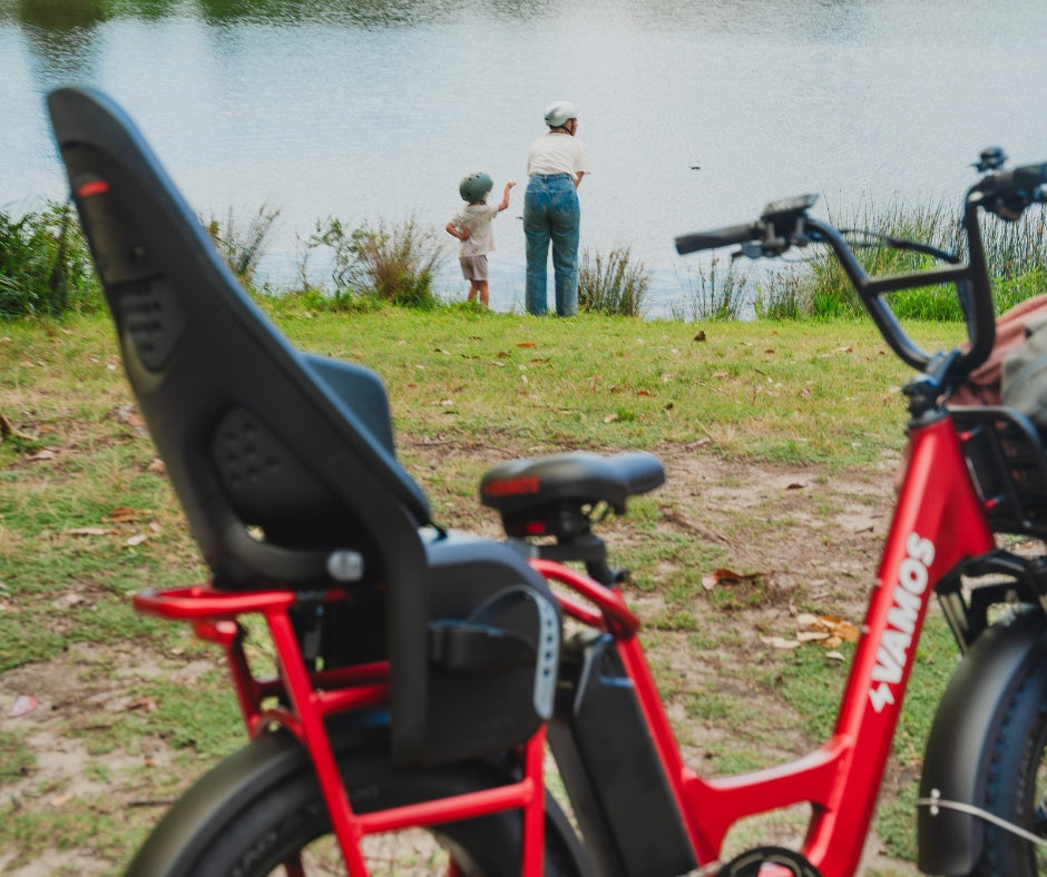 A red Vamos Amigo electric cargo bike equipped with a black Thule Yepp 2 Maxi rear child seat.