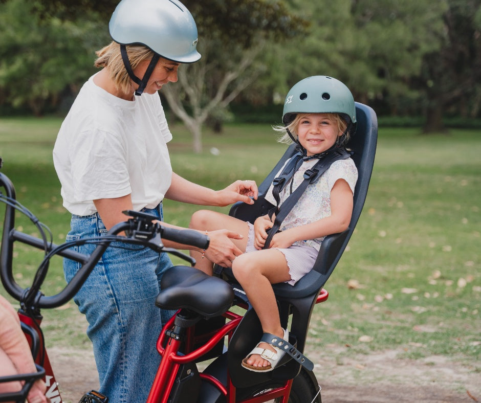 A mother adjusting the harness of a child sitting in a black Thule Yepp 2 Maxi - Child Bike Seat.