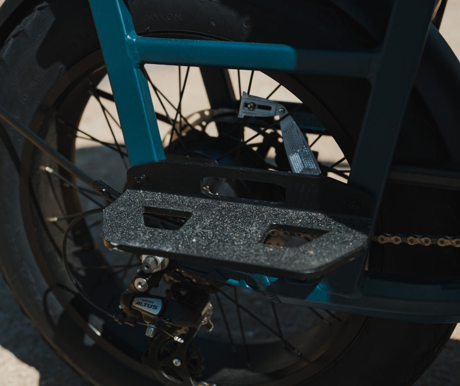 An anti-slip passenger foot peg mounted on the frame of an electric bicycle near a Shimano Altus rear derailleur