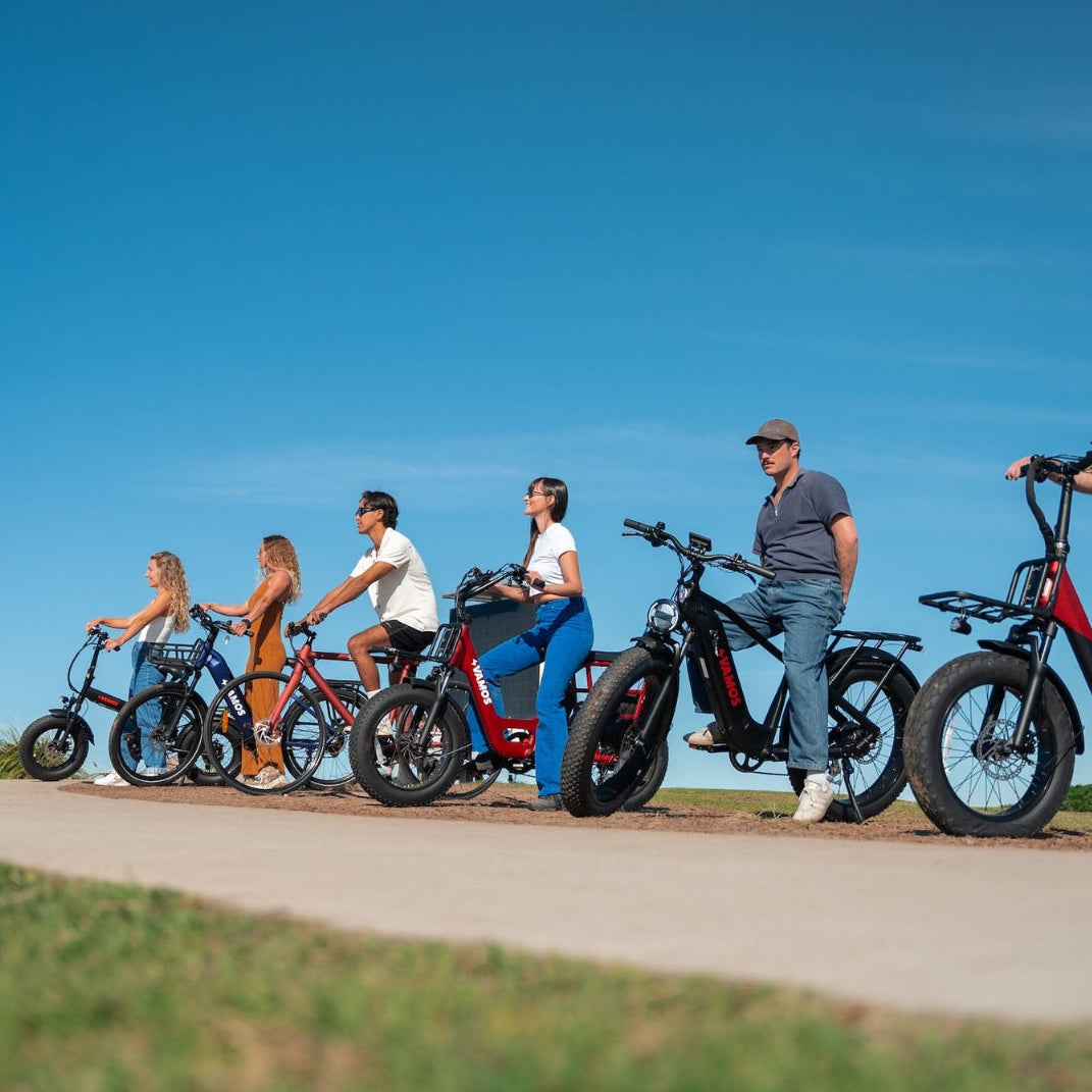 A group of people riding electric fat-tire bikes from Vamos outdoors on a paved path against a clear blue sky