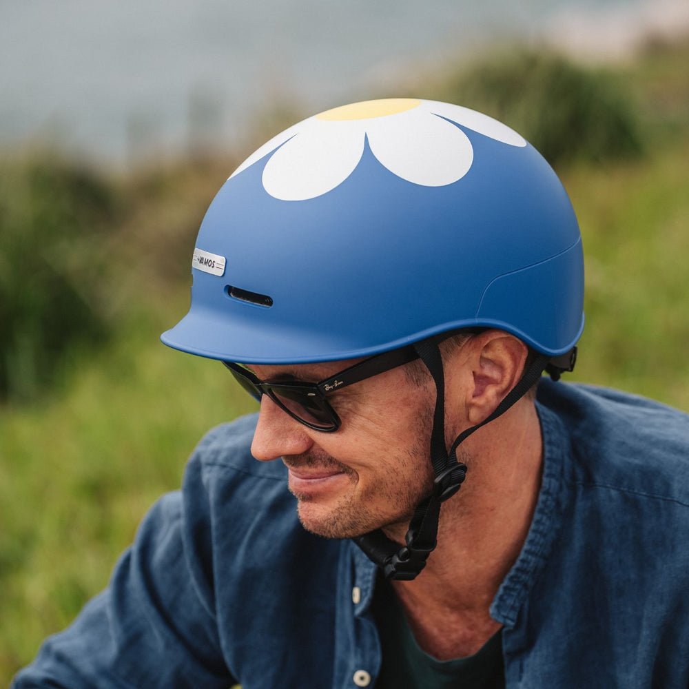 A person wearing a blue Vamos Bike Helmet decorated with a white daisy pattern.