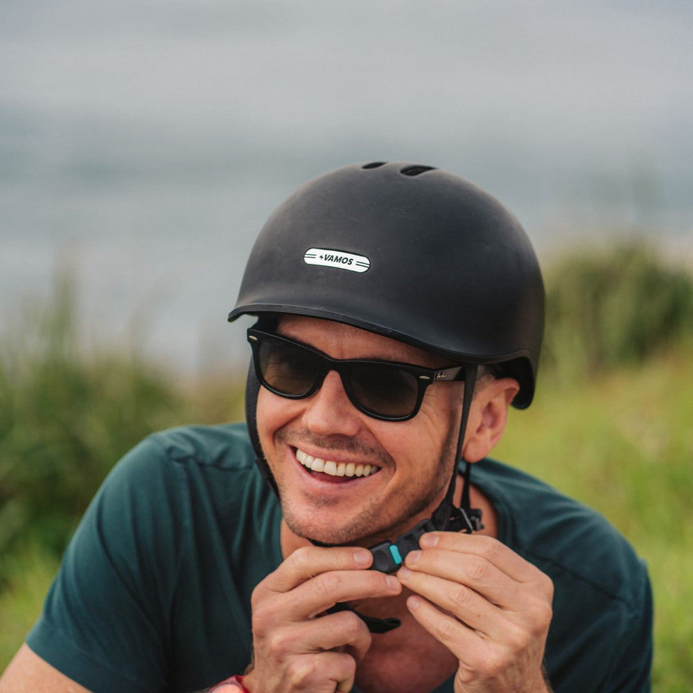 A person adjusting the strap of a Vamos Ebike Helmet in matte black.