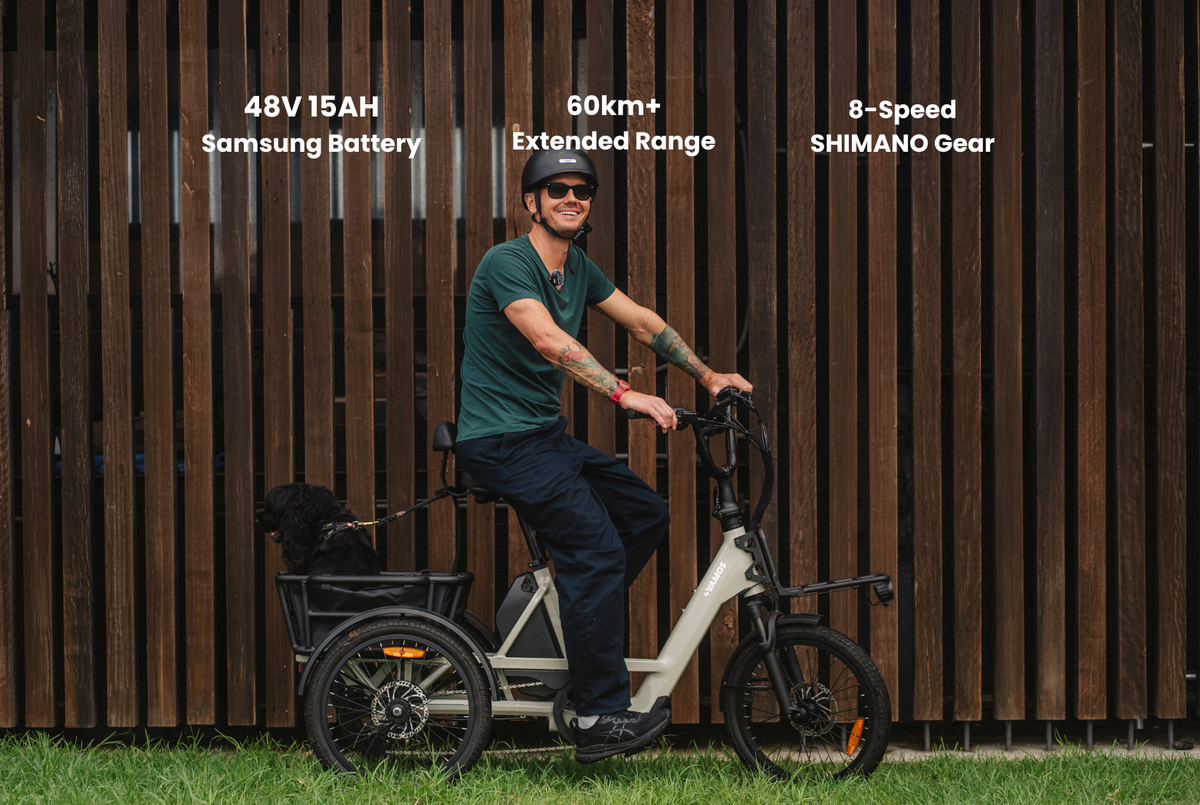 A man smiling while riding a white Vamos Trio, 3 Wheel Electric Trike on grass, featuring a rear cargo basket and tech specs