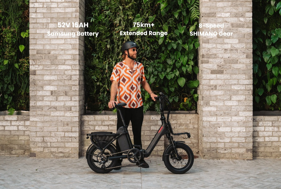 A man in a patterned shirt and helmet stands next to a black Vamos Doblez folding electric bike