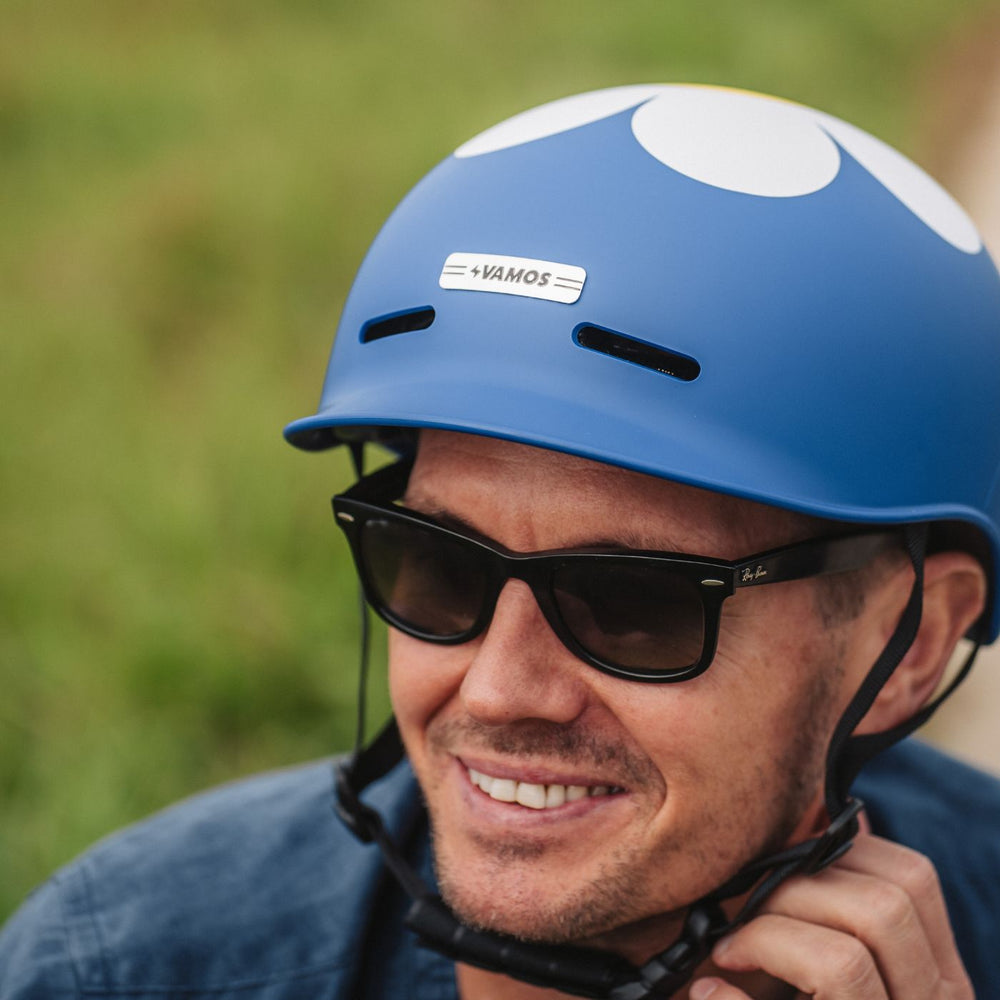 A person wearing a blue Vamos Bike Helmet with a white floral pattern and black sunglasses.