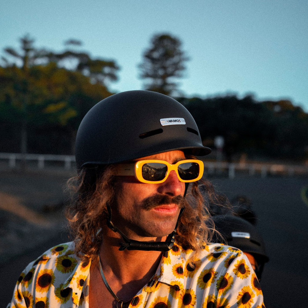 A person wearing a Vamos Bike Helmet with a matte black finish and signature branding detail.