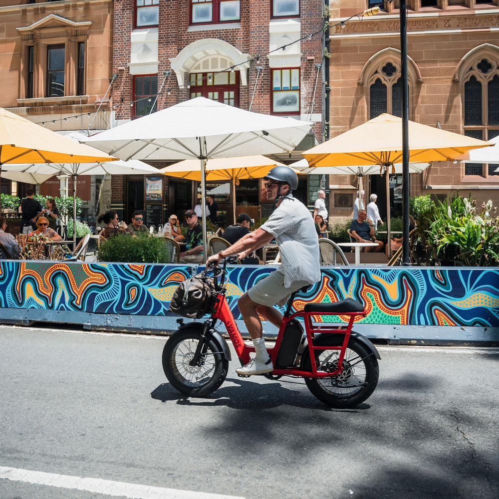 A person riding a red Vamos El Amigo compact cargo e-bike.