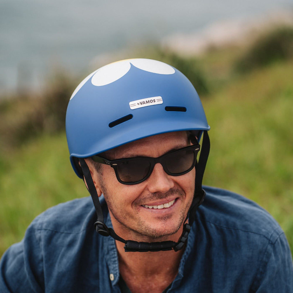 A person wearing a blue Vamos e-bike helmet featuring a white flower-like graphic and a branded label