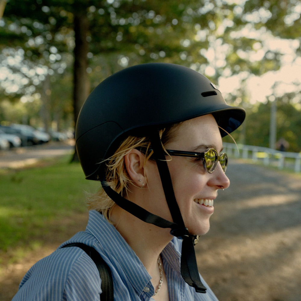 A person wearing a matte black Vamos urban bike helmet with a small integrated visor and black straps.