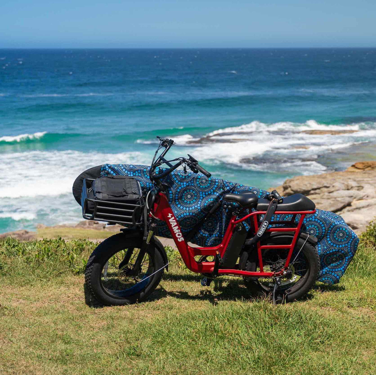 Electric cargo bike parked near the coast carrying a surfboard in a protective cover