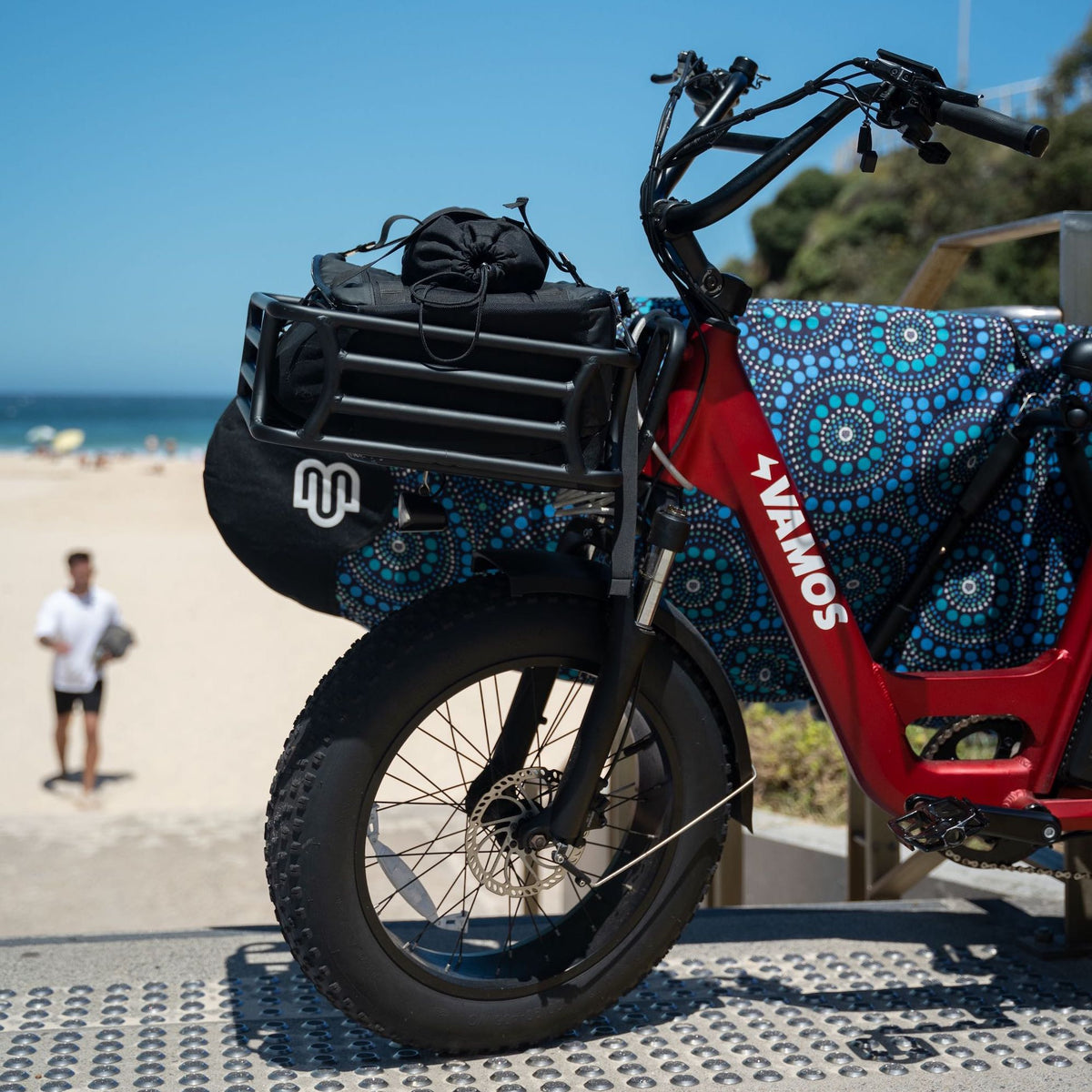 A red Vamos El Amigo compact cargo electric bike parked near a beach.