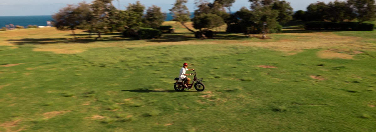 A person riding a compact fat-tire electric bike across an open grassy field.