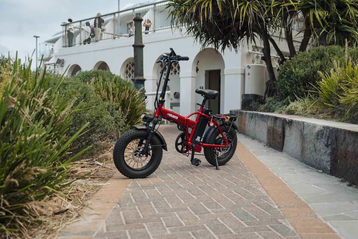 A red Vamos El Doblez folding fat-tire electric bike parked on a paved walkway.