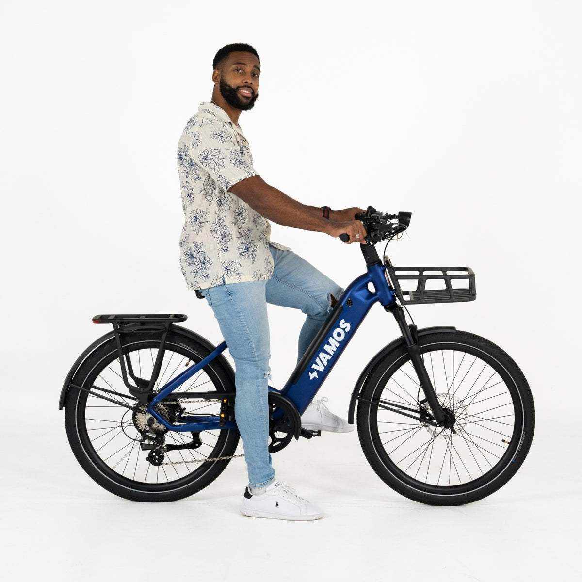 A man with a beard sits on a blue Vamos Rapido 2026 Daily Commuter E-Bike with a front basket against a white background.