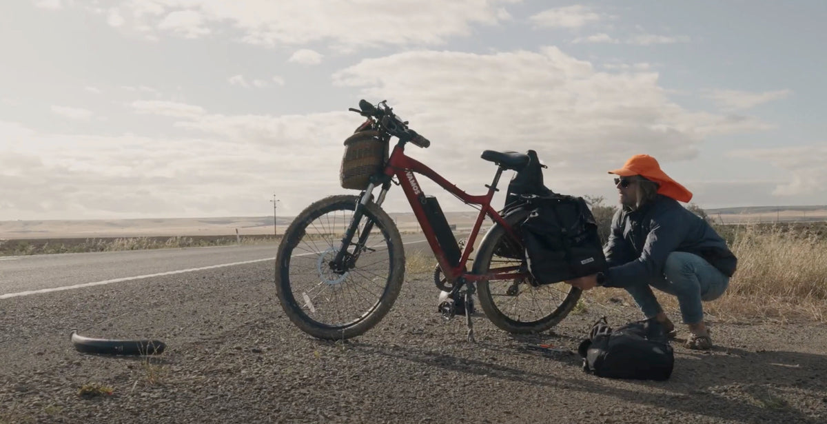 A red Vamos electric bicycle packed with gear on the side of a road.