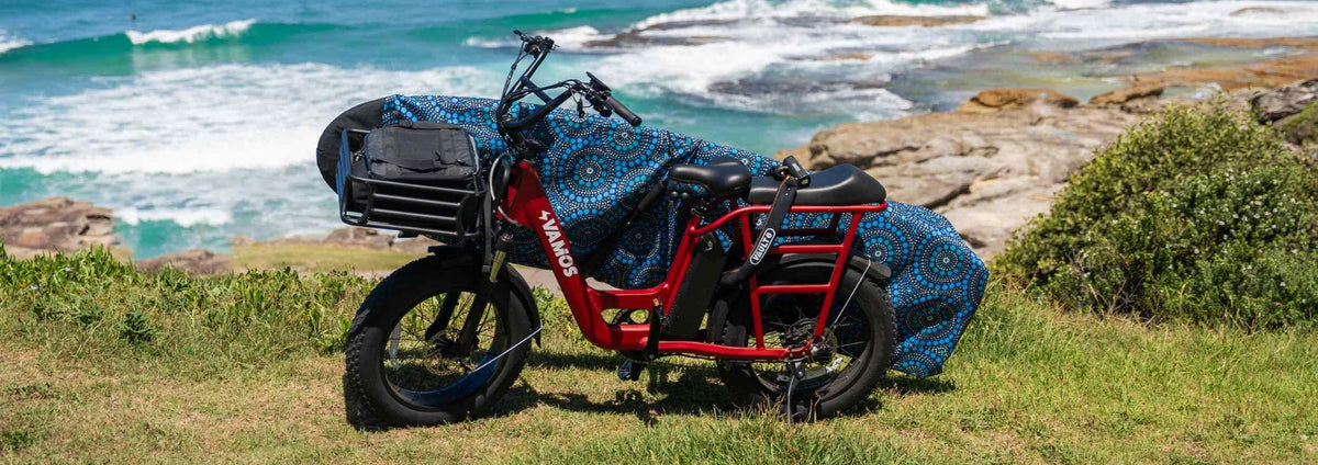 Electric cargo bike parked near the coast carrying a surfboard in a protective cover