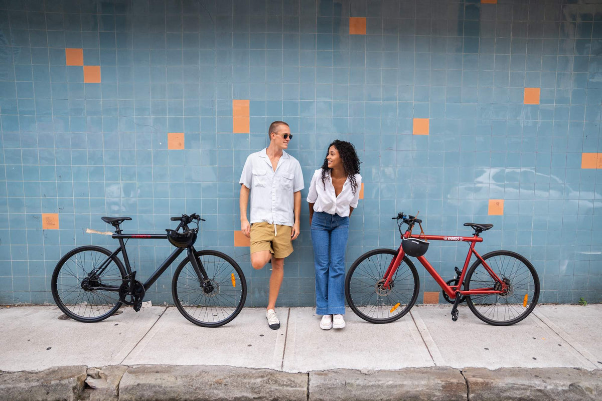 Two people in an urban lifestyle scene with Pluma 2024 Lightweight Flatbar Urban Road Ebike
