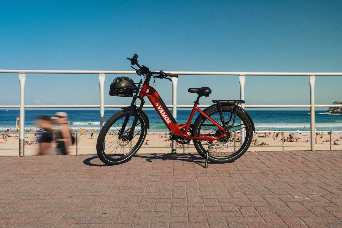 A red Vamos El Rapido commuter e-bike parked near a coastal boardwalk.