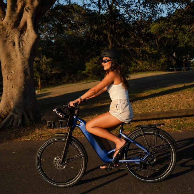 A woman in a white shirt and green cap stands with a blue Rapido City Daily commuter Ebike