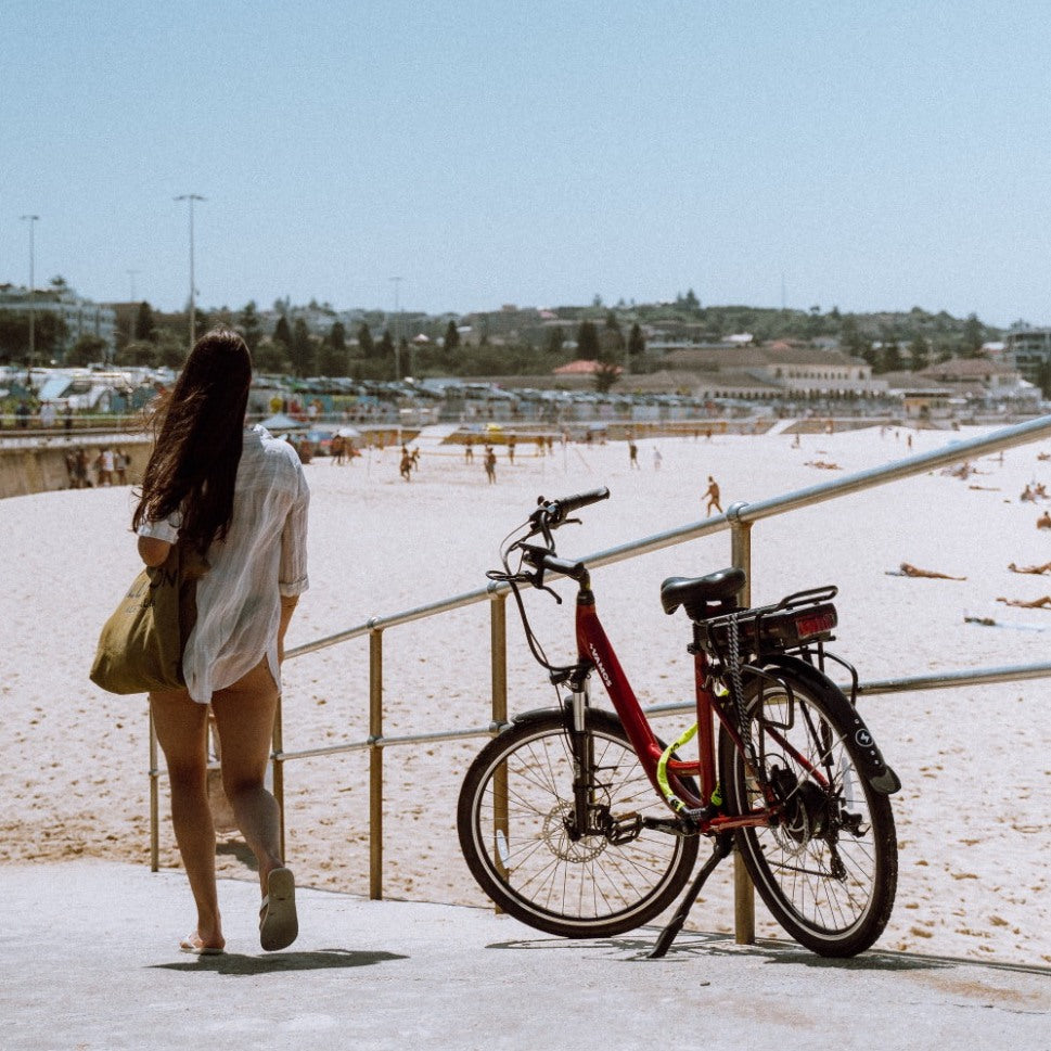 A lady waking towards a beach next to a parked Vamos Rapido Daily Commuter Ebike