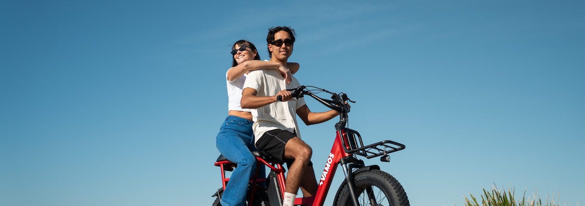 A red Vamos Amigo compact cargo electric bike carrying two riders.