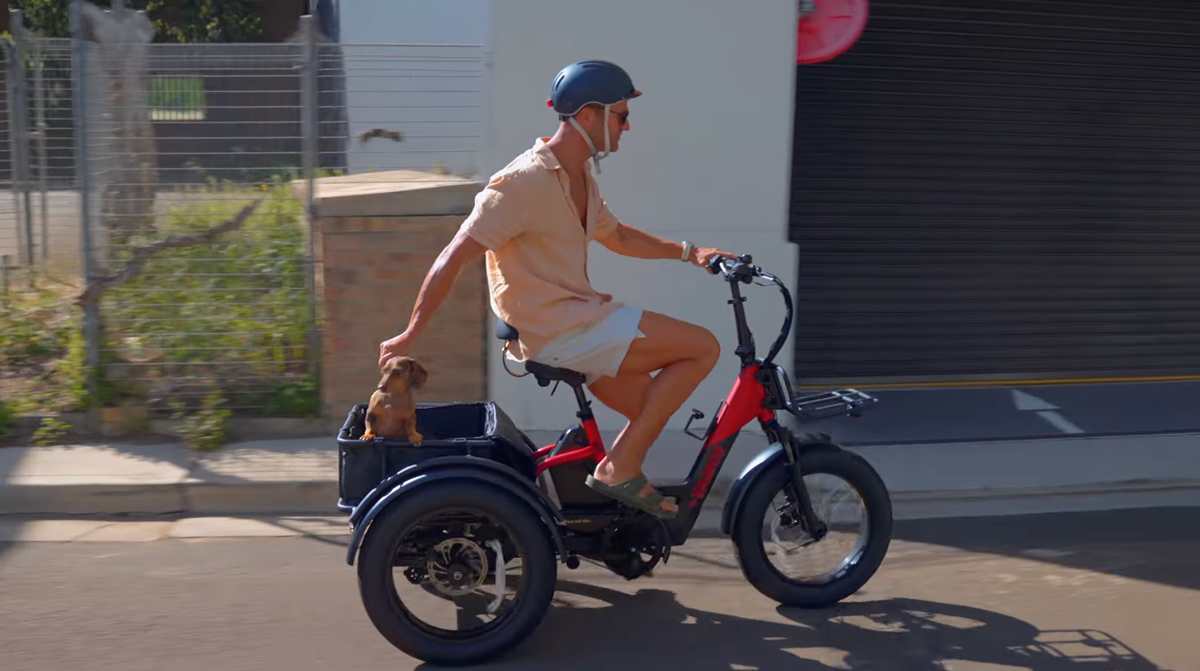 A man wearing a casual attire riding a Red Papa Grande Pro 3-Wheel Electric Bike with fat tires and a large rear cargo basket