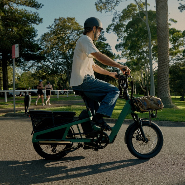 Man wearing a helmet riding a green Vamos El Amigo Plus Commuter Ebike on a paved park path
