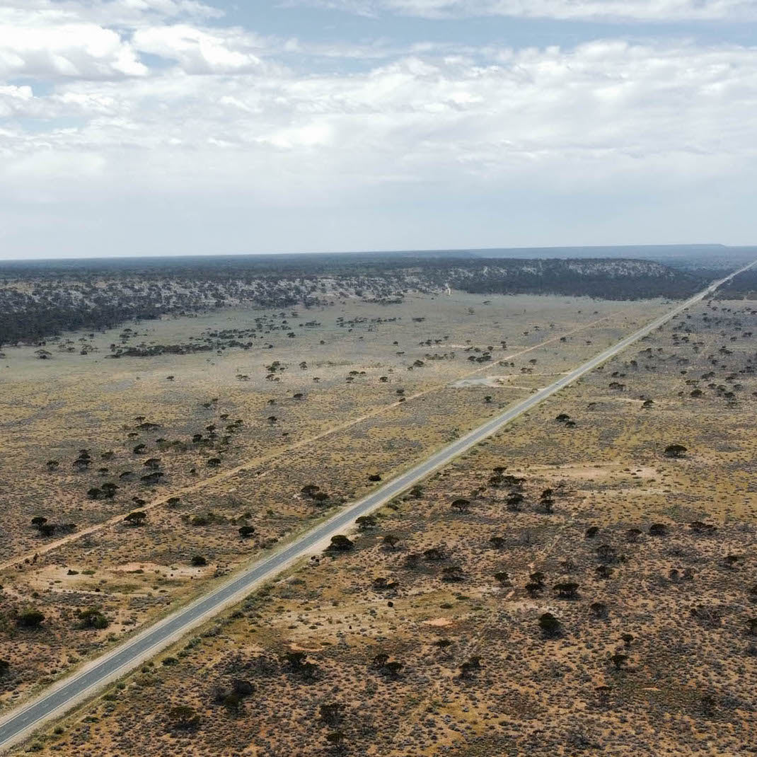 A long, straight stretch of the Eyre Highway cutting across the flat, arid landscape of the Nullarbor Plain in Australia