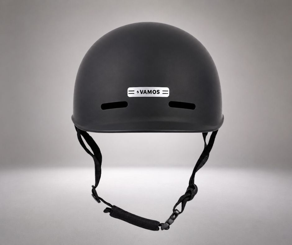 A matte black Vamos bike helmet featuring a sleek silver logo badge on the front.