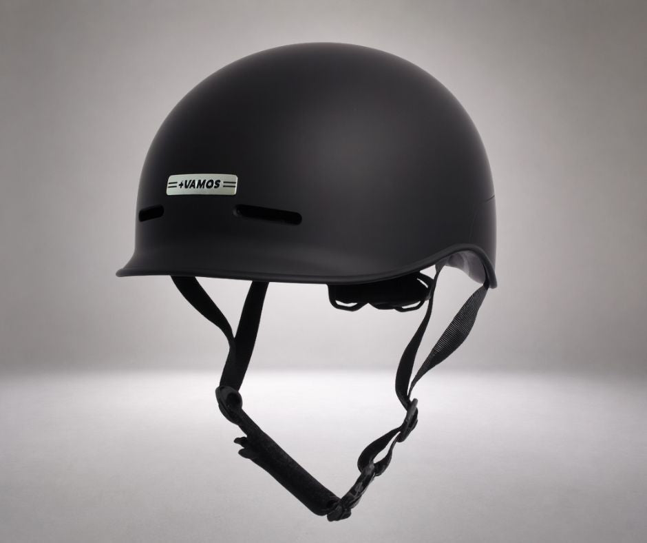A matte black Vamos bike helmet featuring a distinctive silver logo plate on the front.