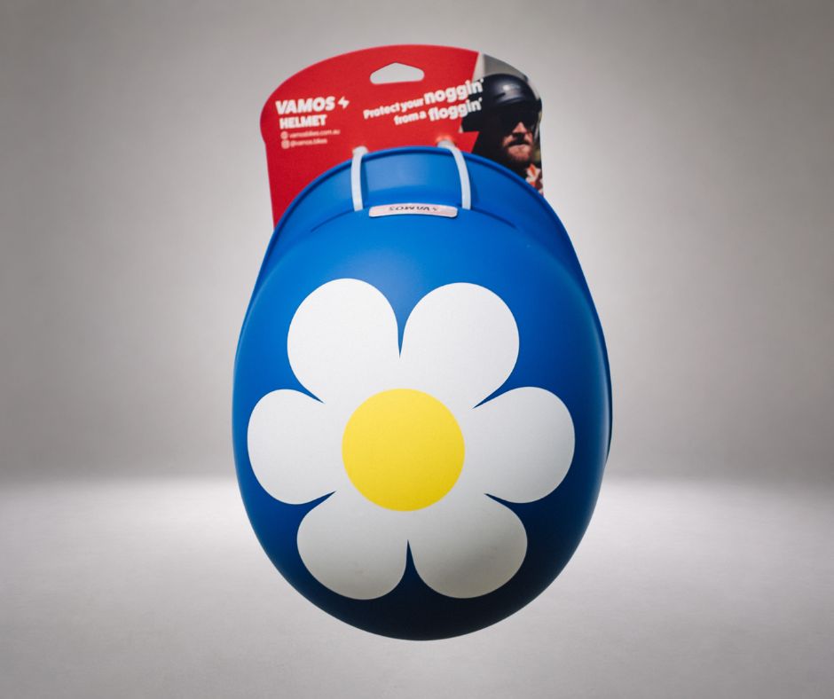 A blue vamos helmet featuring a large white and yellow daisy flower graphic on the front.