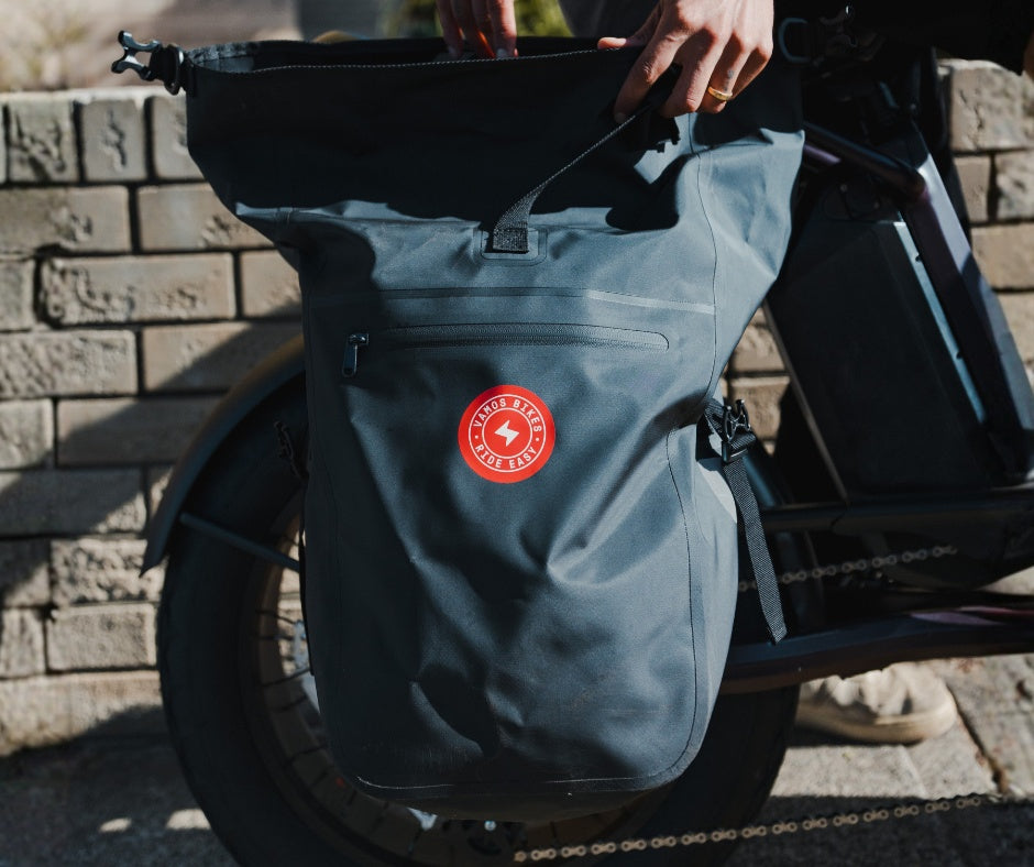 A hands-on view of a dark grey Vamos Waterproof Pannier Bag for Bike with Quick Release Mount attached to a bicycle rack.