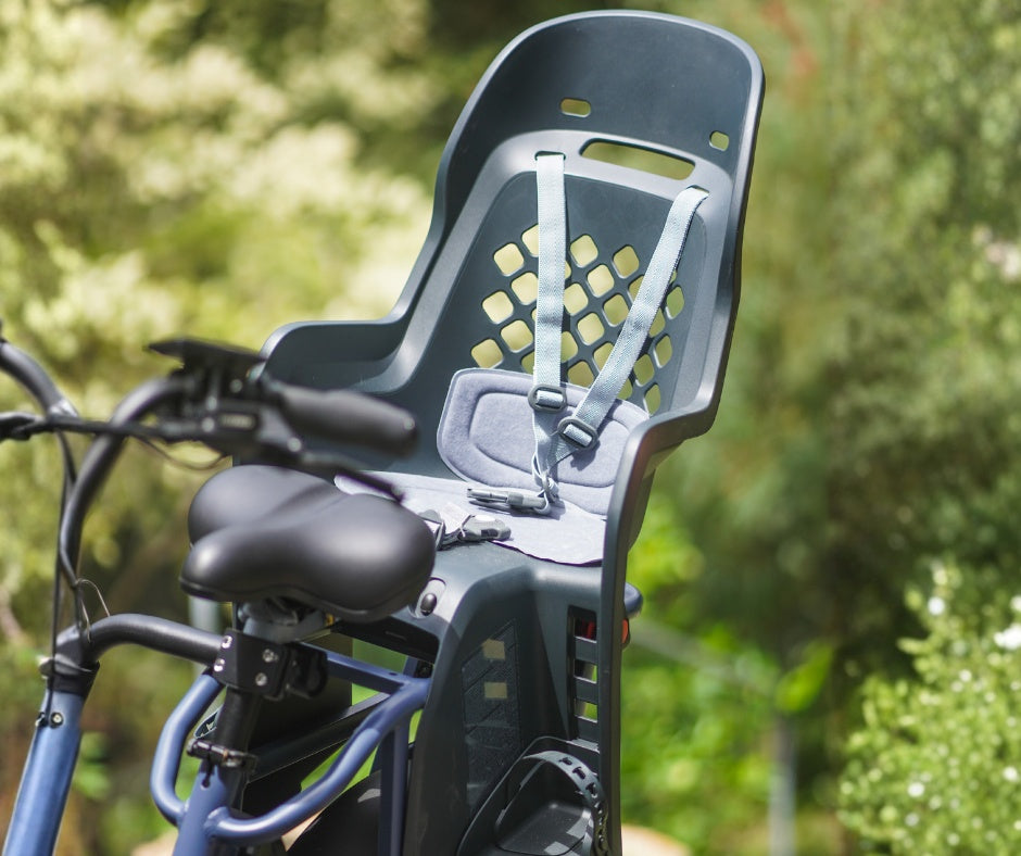 A dark gray Thule Yepp 2 Maxi Child Bike Seat mounted on the back of a blue bicycle outdoors.