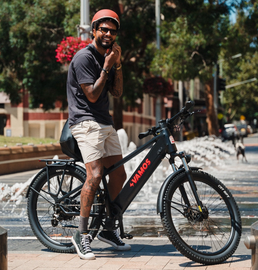 Rider standing beside a fat-tyre electric bike in an urban plaza with water feature