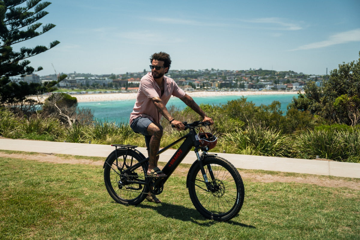A man riding an El Rapido Commuter Ebike onm a grassy hill overlooking the ocean