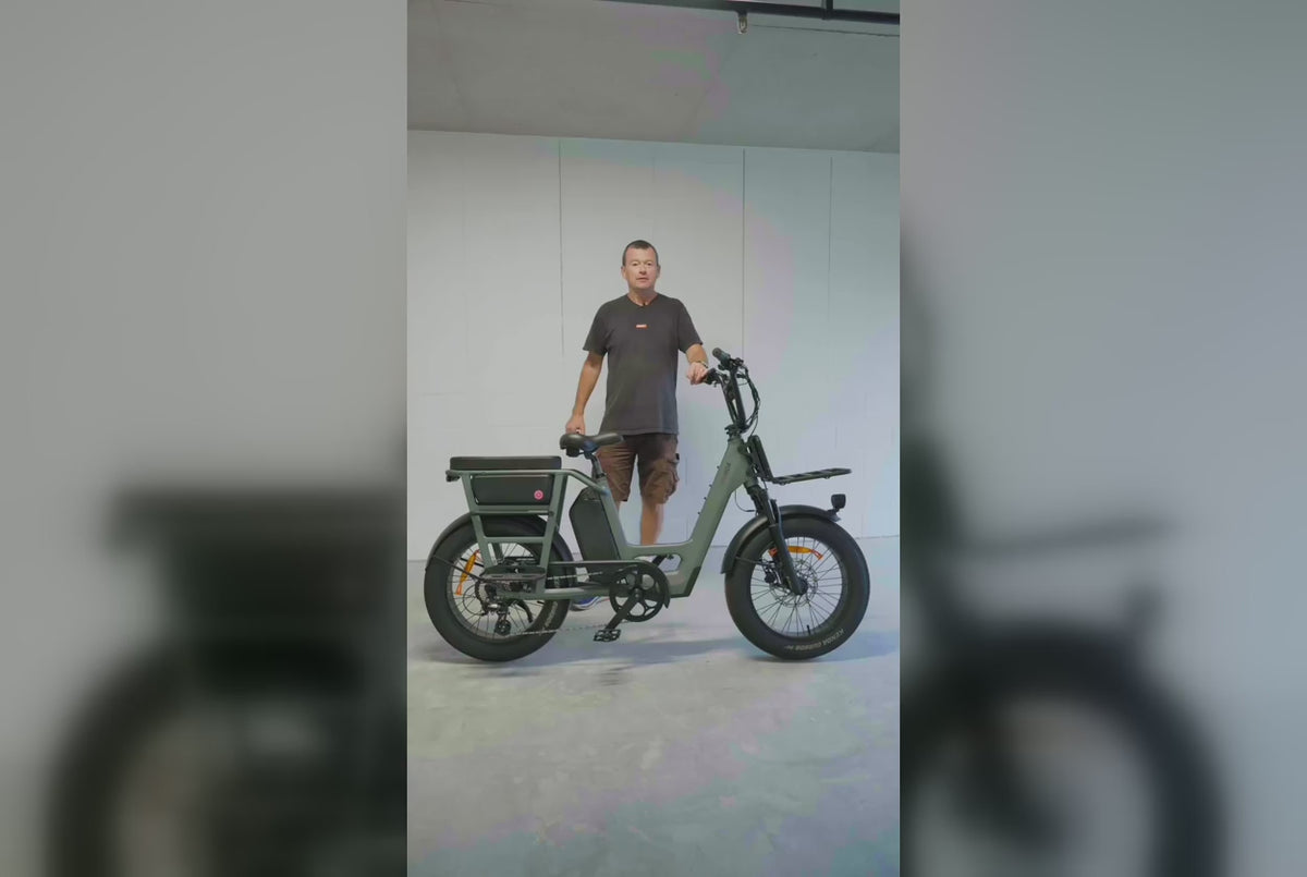 Man standing next to a grey-green Vamos electric bike in front of a white wall.