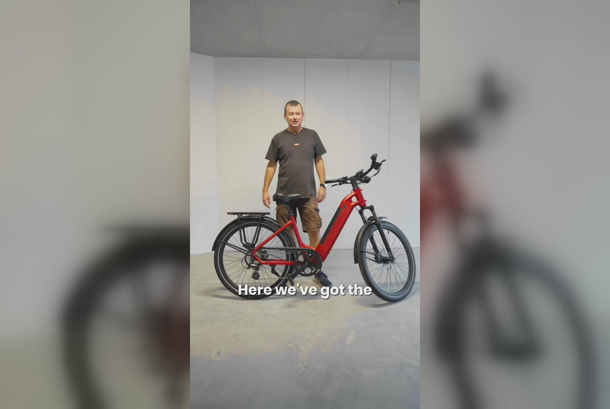 Man standing behind a red Vamos electric bicycle against a white wall.