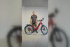 Man standing behind a red Vamos electric bicycle against a white wall.