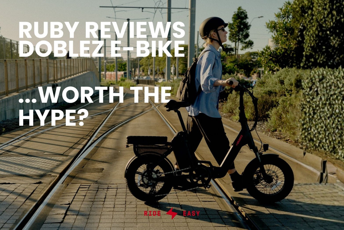Woman wearing a helmet pushing a black Vamos Doblez electric bike across tram tracks.