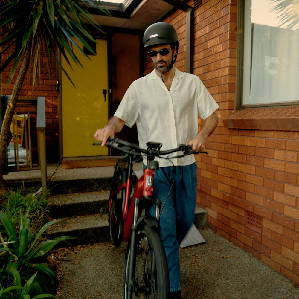 Man walking red Vamos electric commuter bike outside brick residential home.