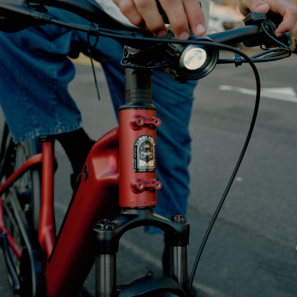 Close-up of red Vamos e-bike head tube badge, front suspension fork, and bright LED headlight.