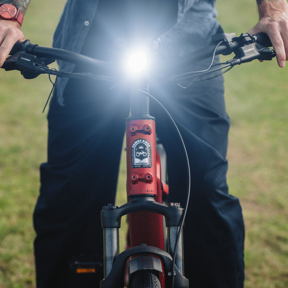 Front angle view of red Vamos e-bike featuring illuminated LED headlight and branded frame crest.