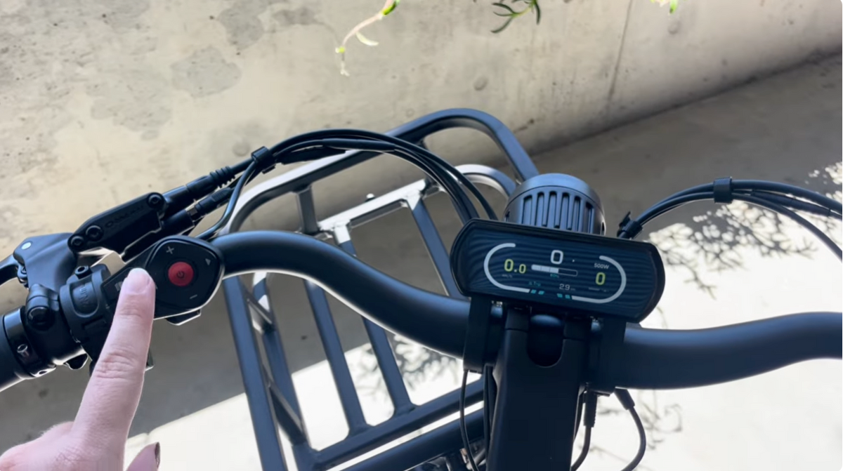 Point-of-view close-up of handlebar controls and digital LCD display screen on a Vamos electric bike.