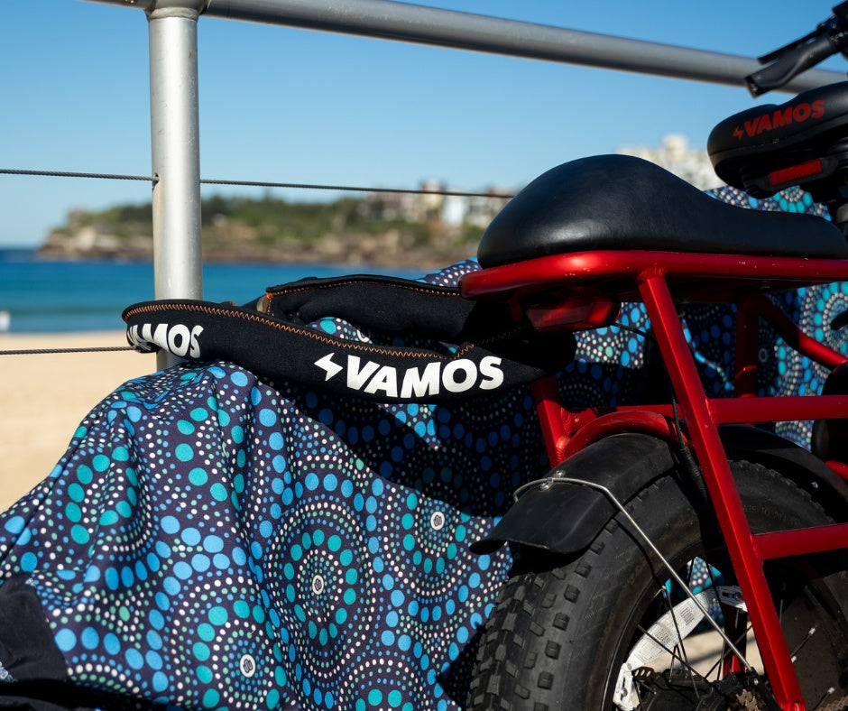 A red Vamos Bikes electric bicycle equipped with a branded Vamos Combination Chain Lock resting near a patterned textile